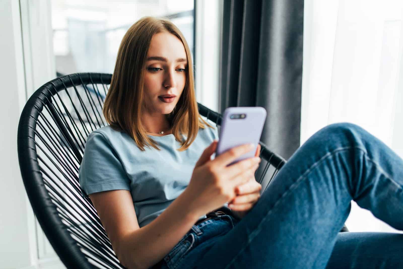donna in camicia blu che usa lo smartphone mentre è seduta sul divano