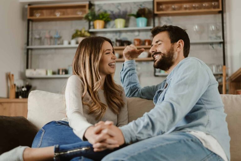 um casal sorridente sentado no sofá a rir enquanto dá as mãos