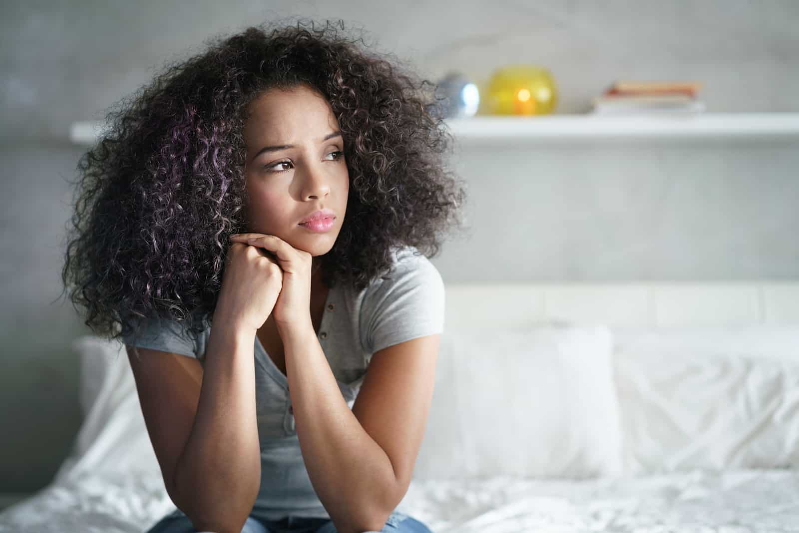 a disappointed woman with frizzy hair is sitting on the bed
