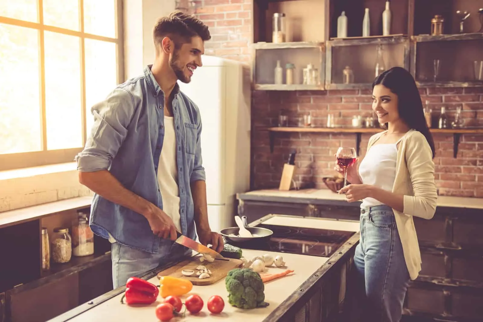 Beautiful young couple is talking and smiling while cooking in kitchen at home