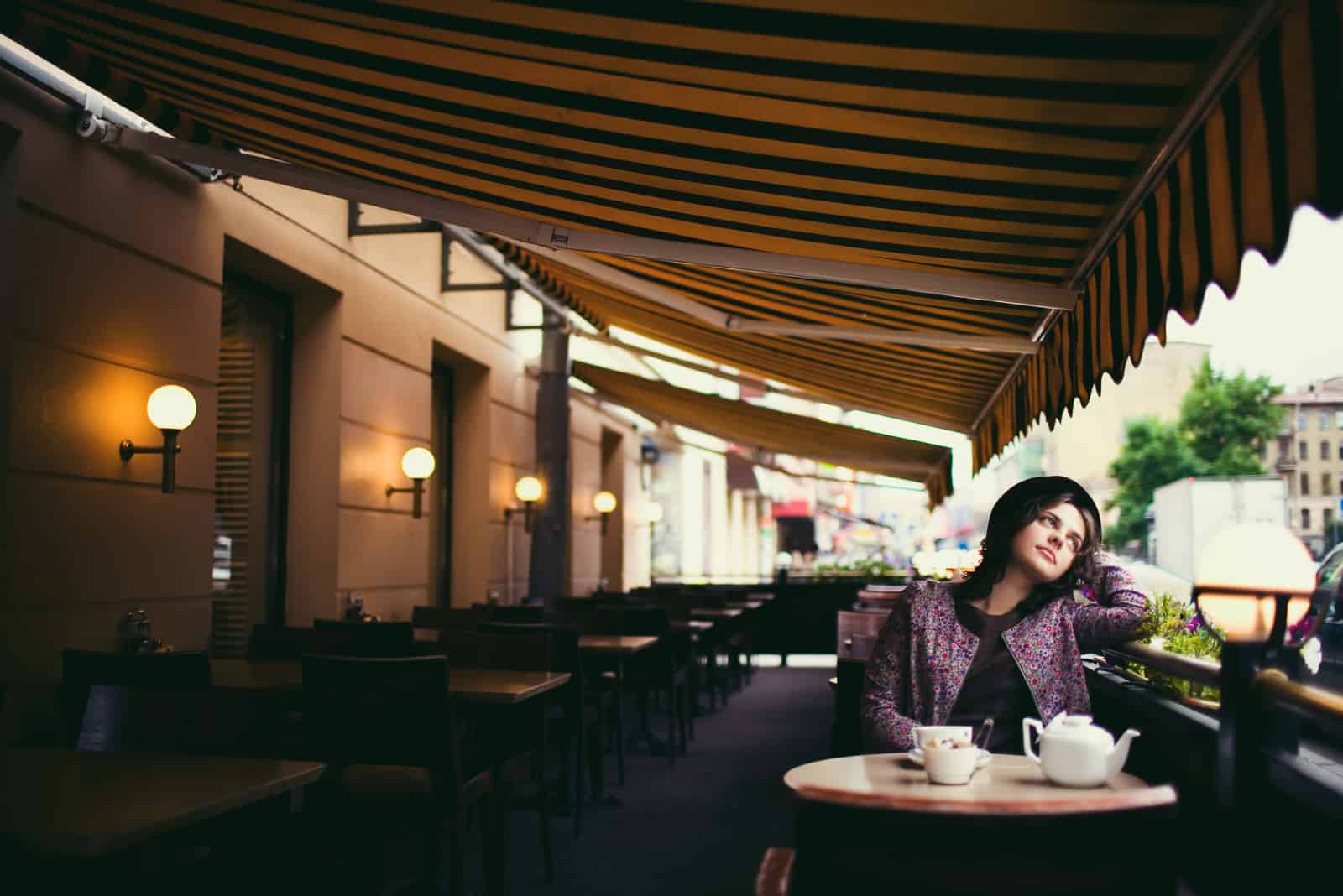 Bella donna giovane con un cappello e una tazza di tè seduta in un caffè, guardando le persone che passano