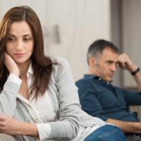 sad woman turning from husband sitting on sofa and watching tv