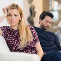 pensive woman turning head from her boyfriend who uses smartphone