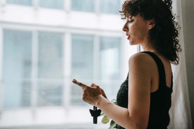 woman holding smartphone while standing near window