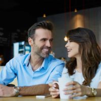 man and woman smiling while sitting in cafe