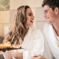 joyful couple in love holding plate with fruit in bedroom