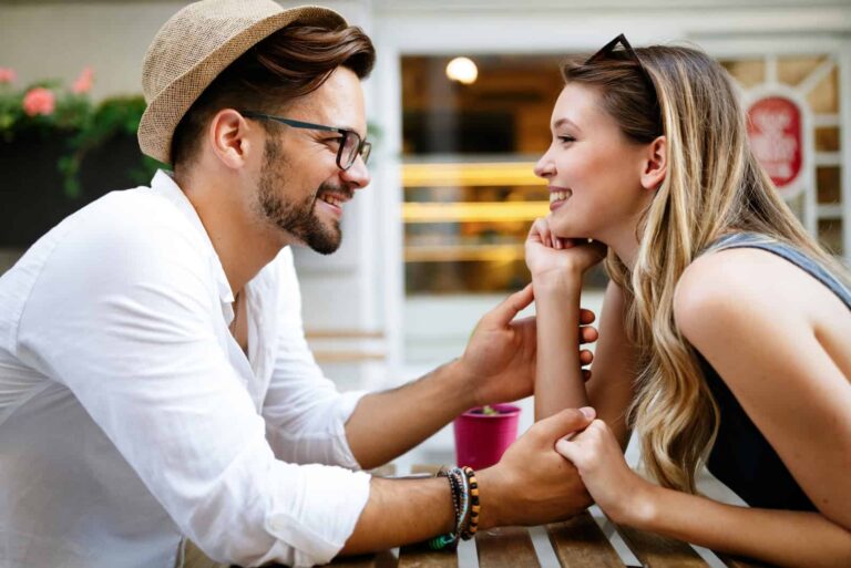happy man holding woman's hands while sitting at table