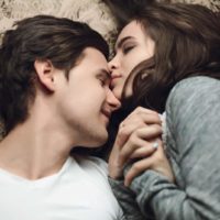 woman kissing man on forehead while laying on bed