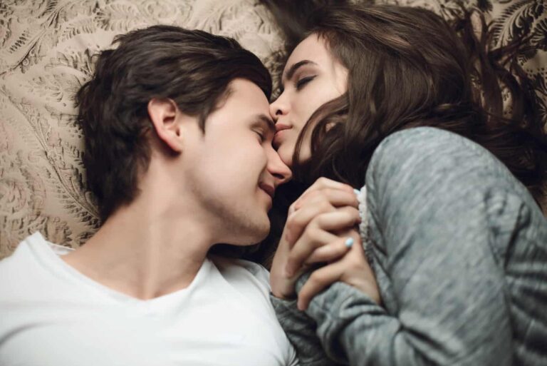 woman kissing man on forehead while laying on bed