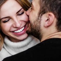 a smiling woman in a man's arms as he kisses her on the cheek