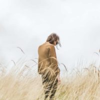 woman in beige sweater standing in the middle of wheat field