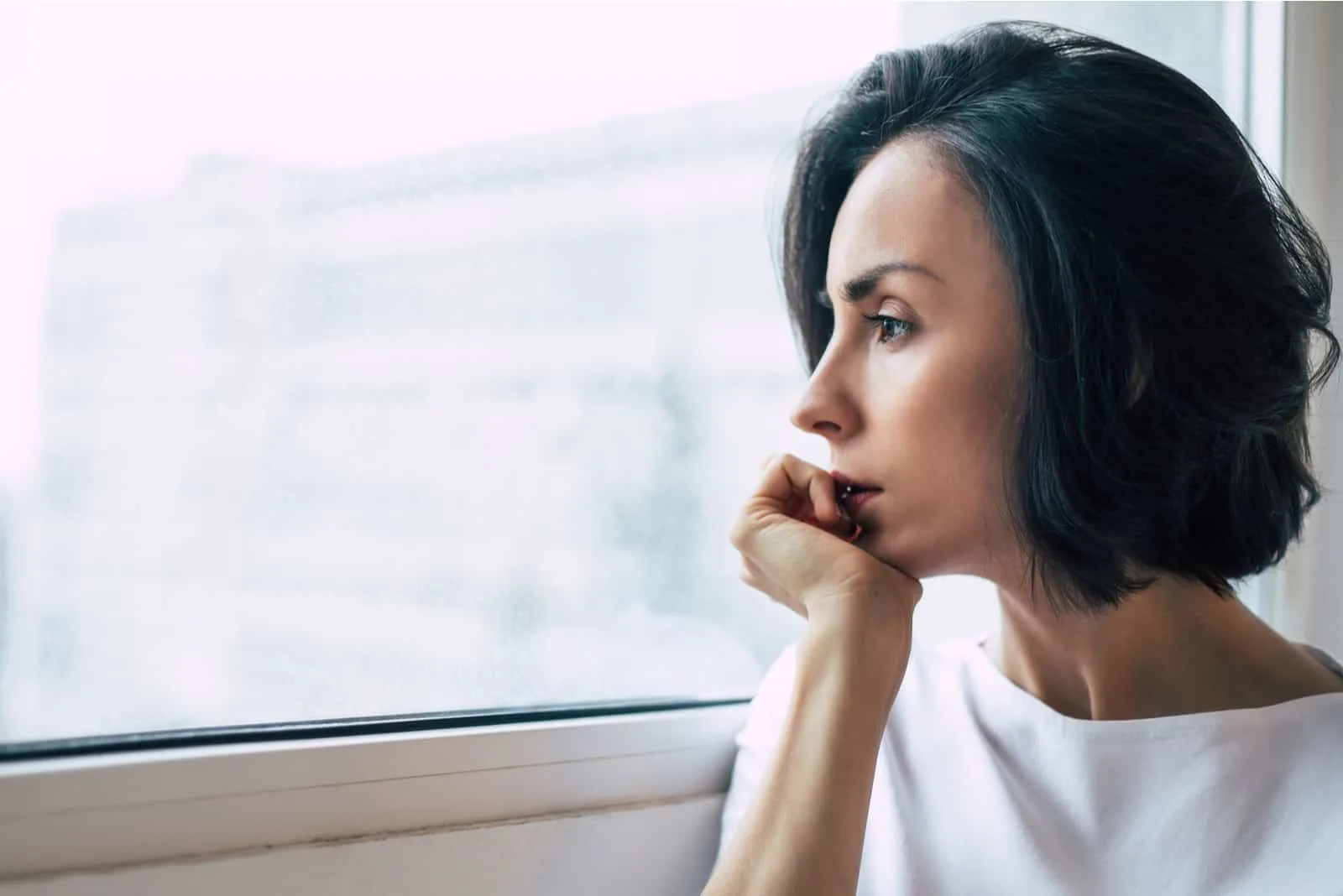 a depressed frightened woman looks out the window