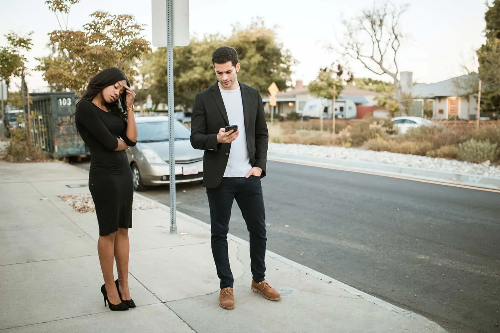 a jealous man checking smartphone of his girlfriend while standing together on the sidewalk