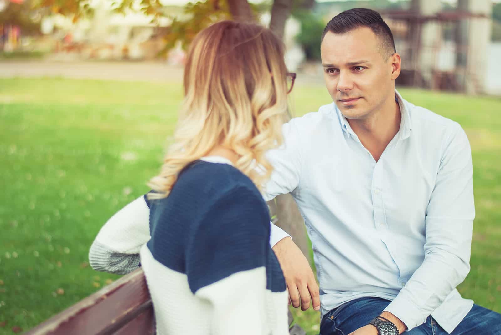 a man and a woman having serious conversation sitting on the bench in the park