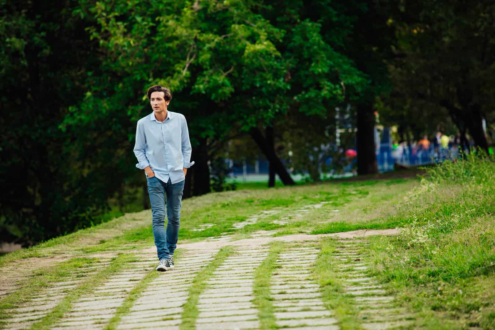 a man in a blue shirt and jeans walks through the park