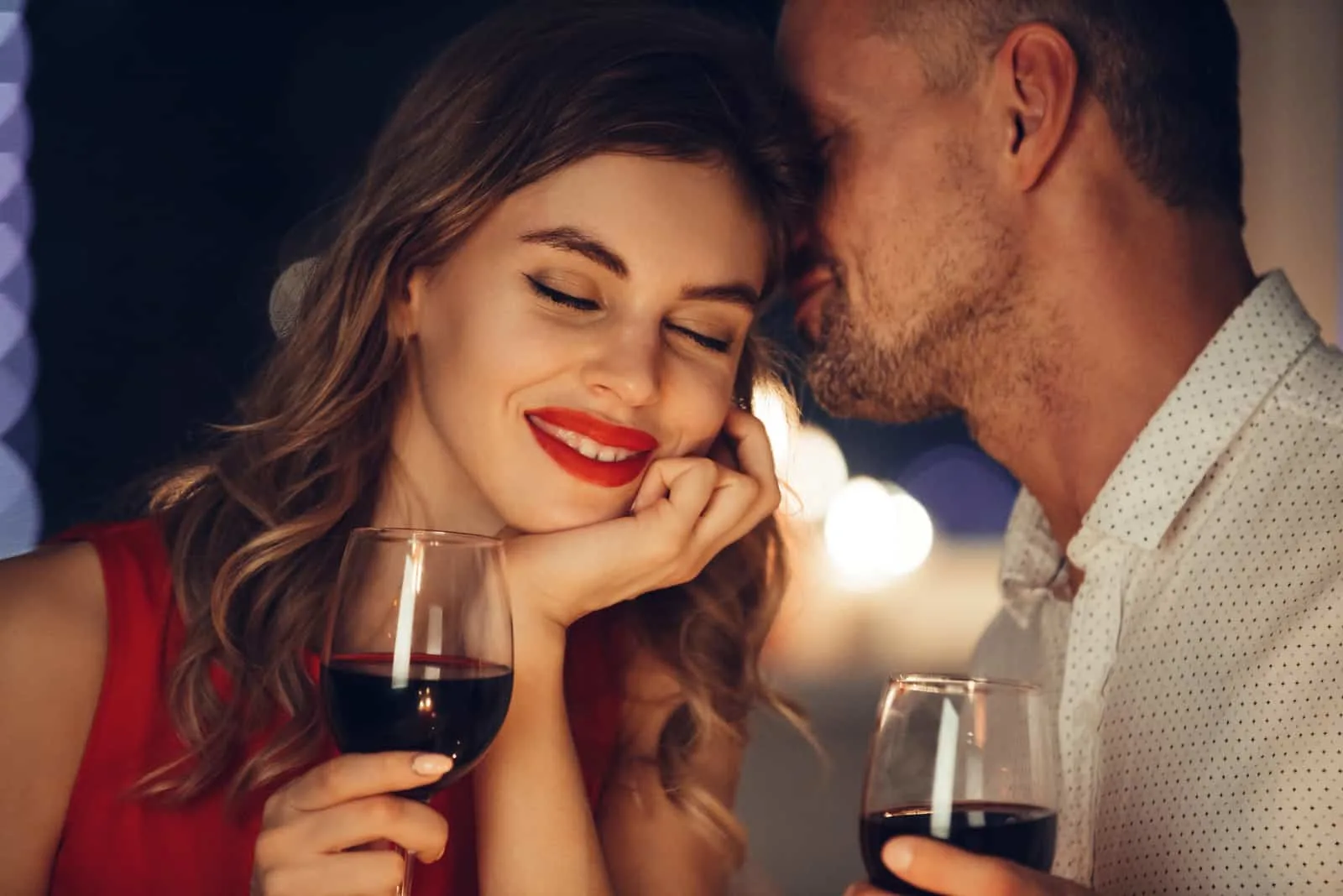 a man whispers in a woman's ear while drinking wine