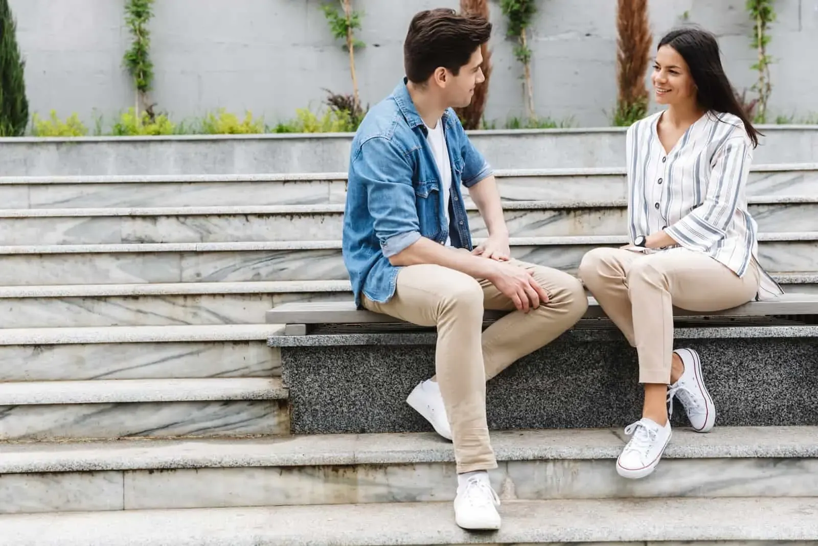 a smiling man and woman sit on a bench and look at each other