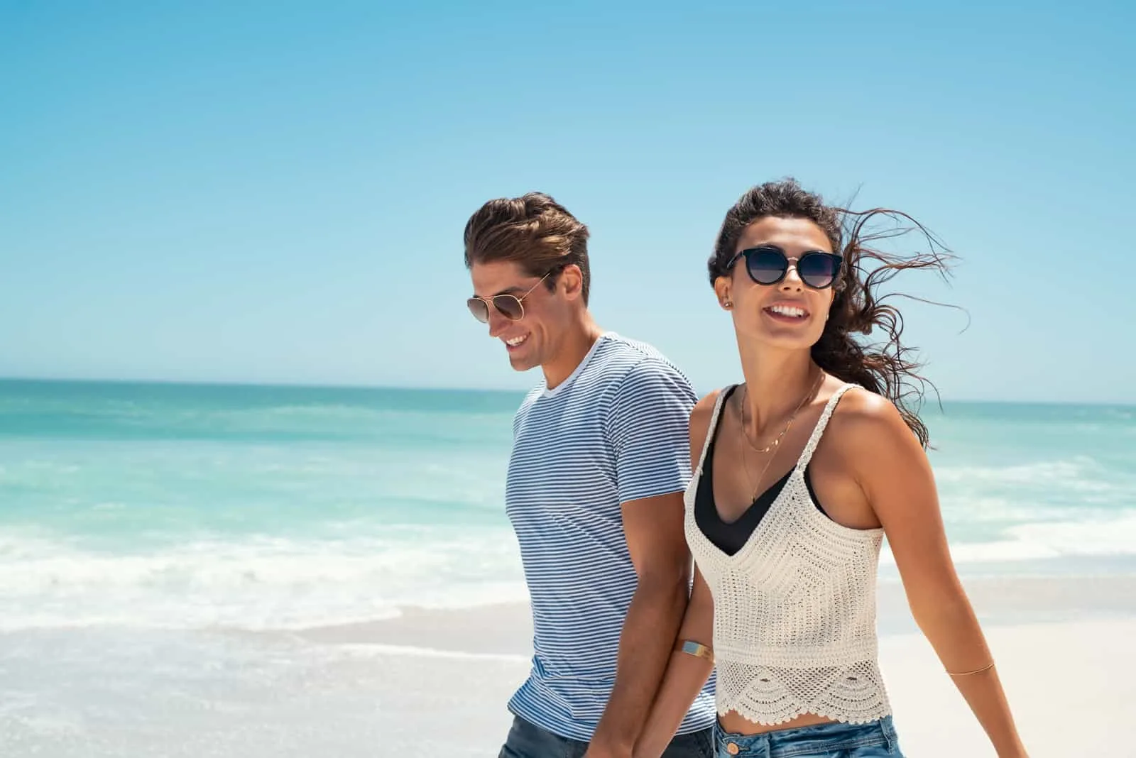 a smiling man and woman walk the beach
