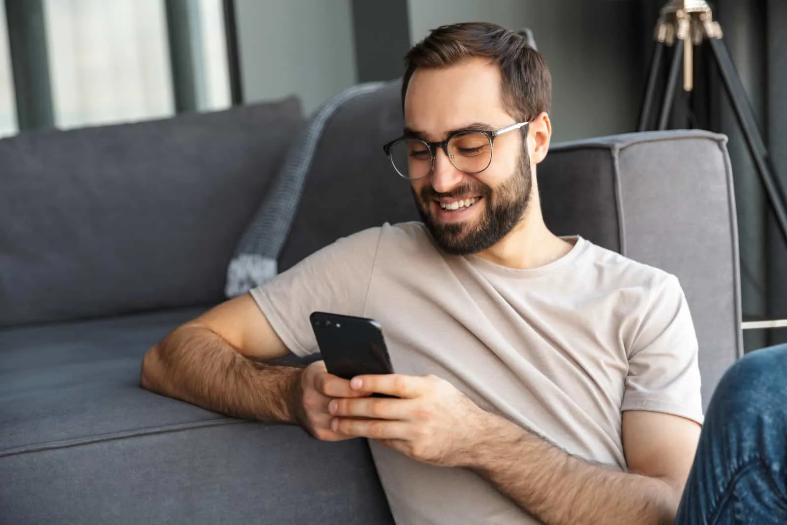 a smiling man sitting on the floor leaning on the couch button on the phone