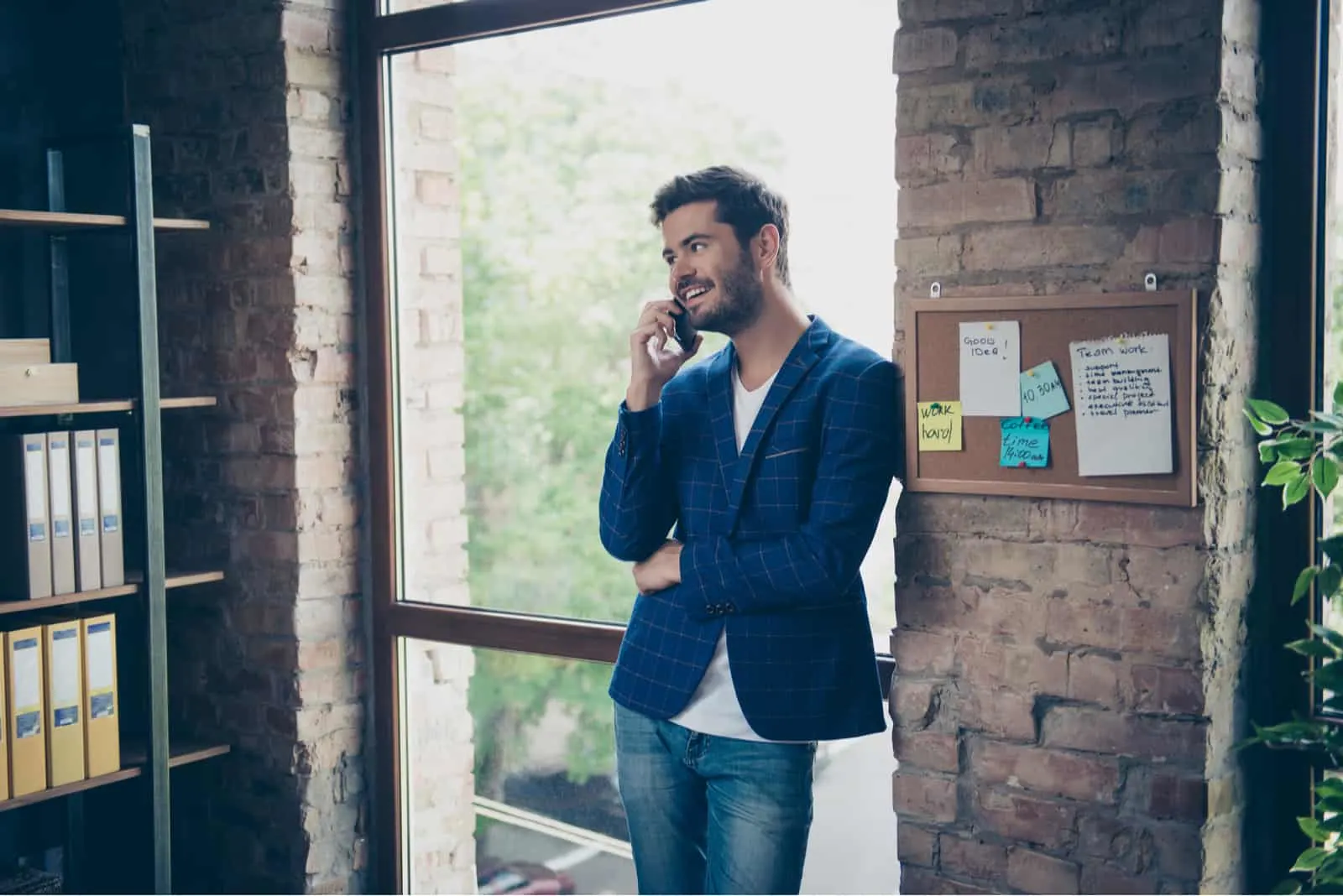 a smiling man stands in the office and talks on the phone