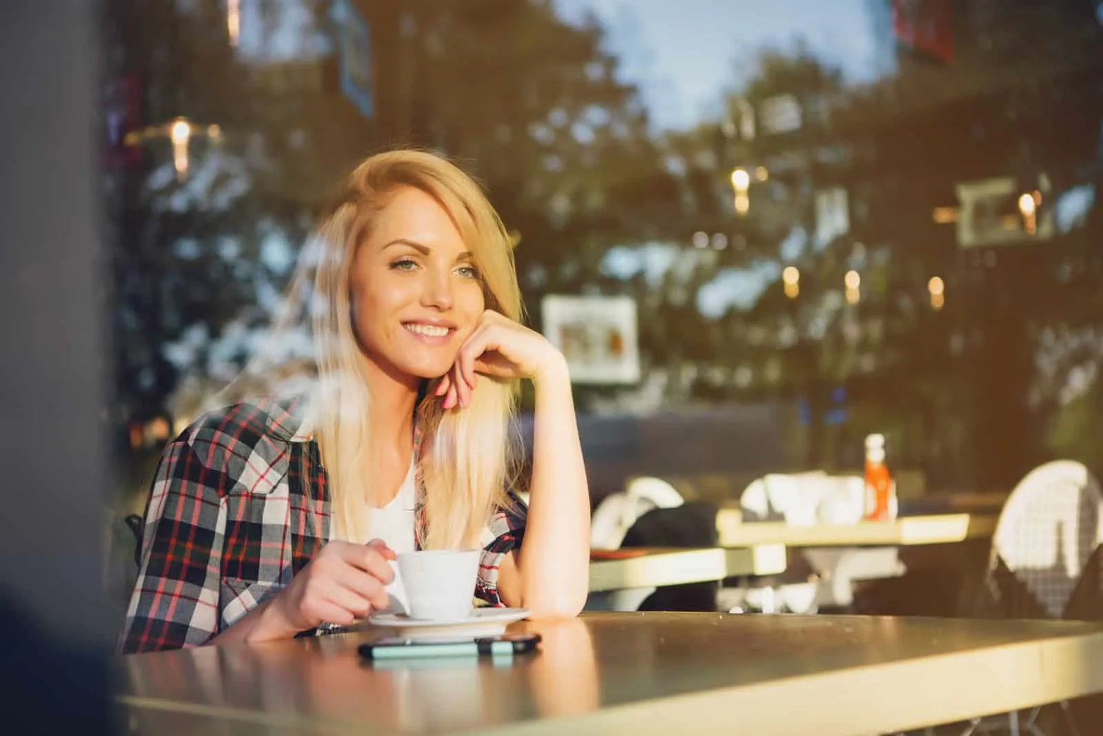 a smiling woman sits in a cafe and drinks coffee