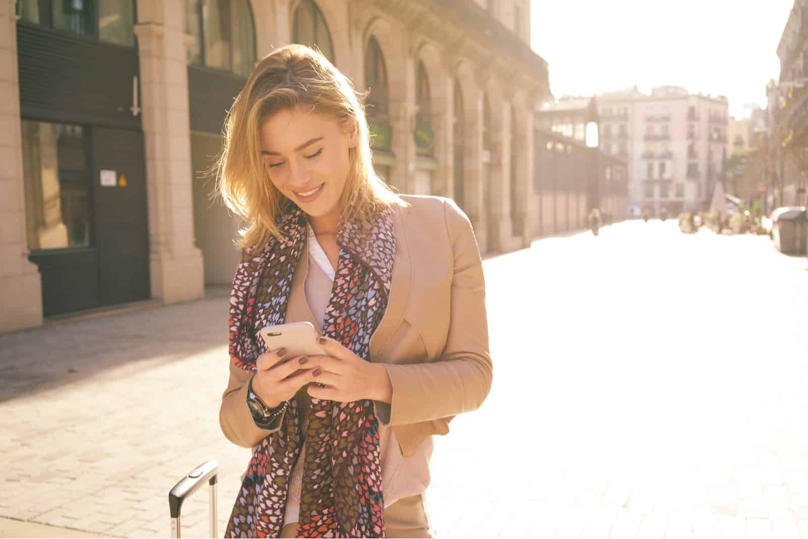 a smiling woman standing on the street and pressing a phone