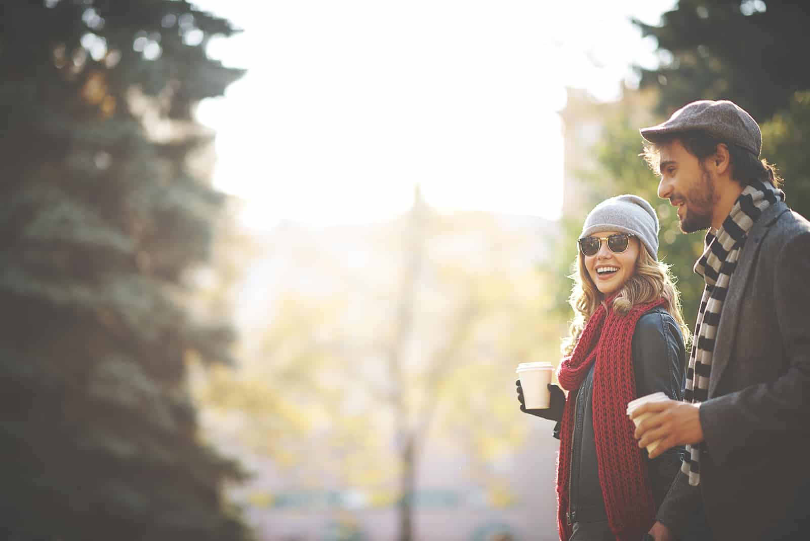 a smiling woman walking with a man and carrying coffee on a date