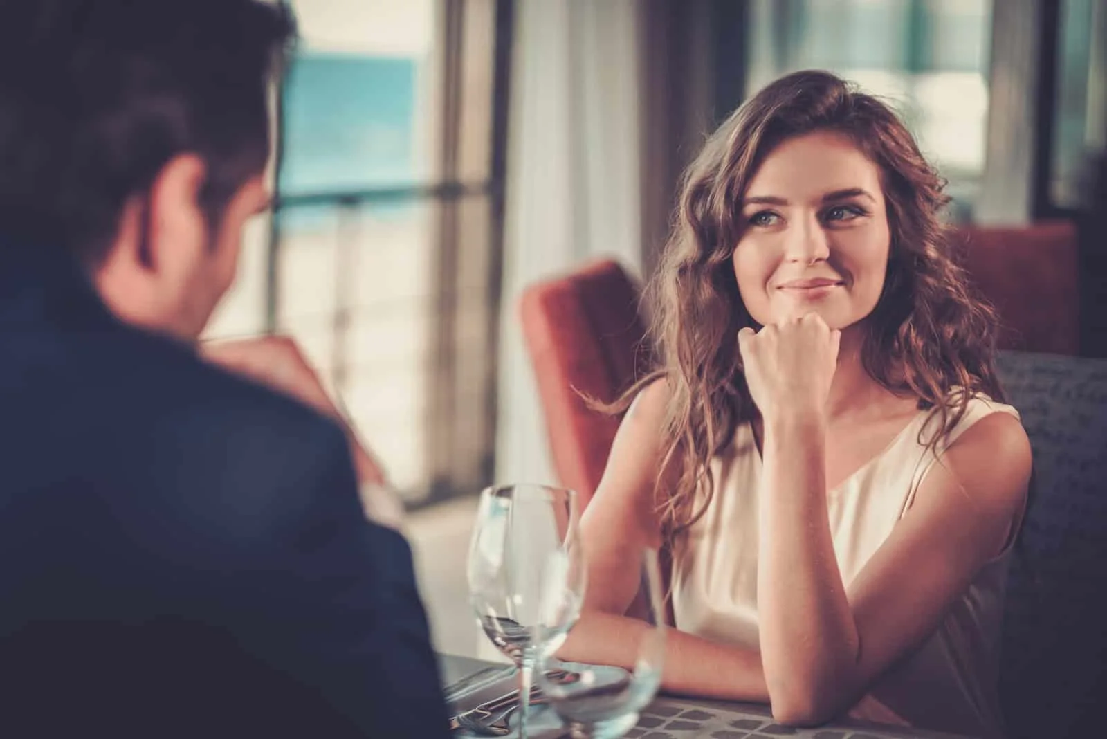 a smiling young couple watching each other as they sit in a restaurant