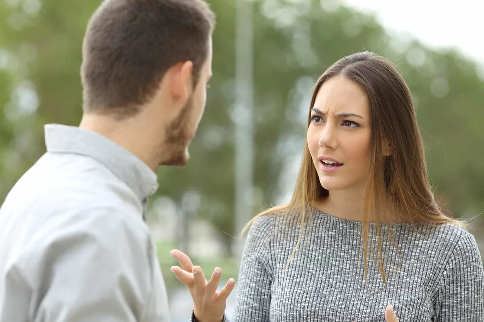 a woman and a man seriously talking while standing in the park