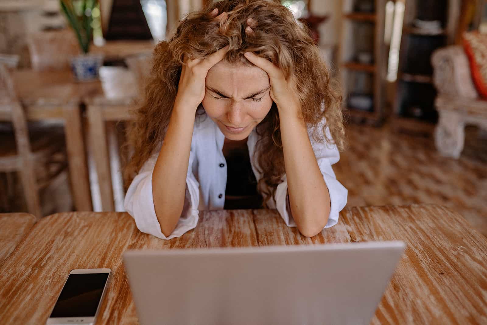 una donna che si tocca la testa con le mani sentendosi stressata mentre è seduta a casa davanti al computer portatile
