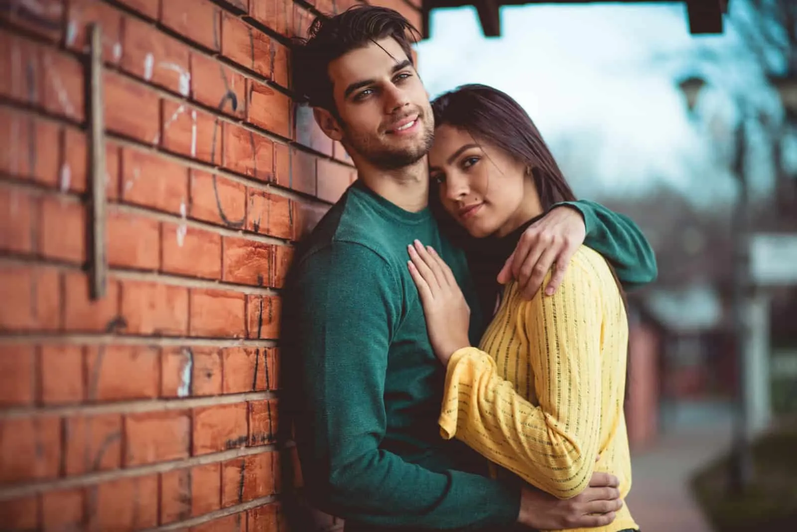 a young attractive couple hugging against a brick wall