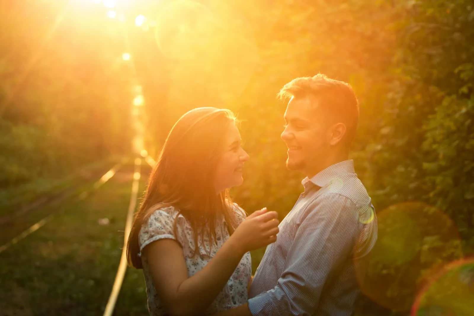 a young couple is hugging in the park at sunset
