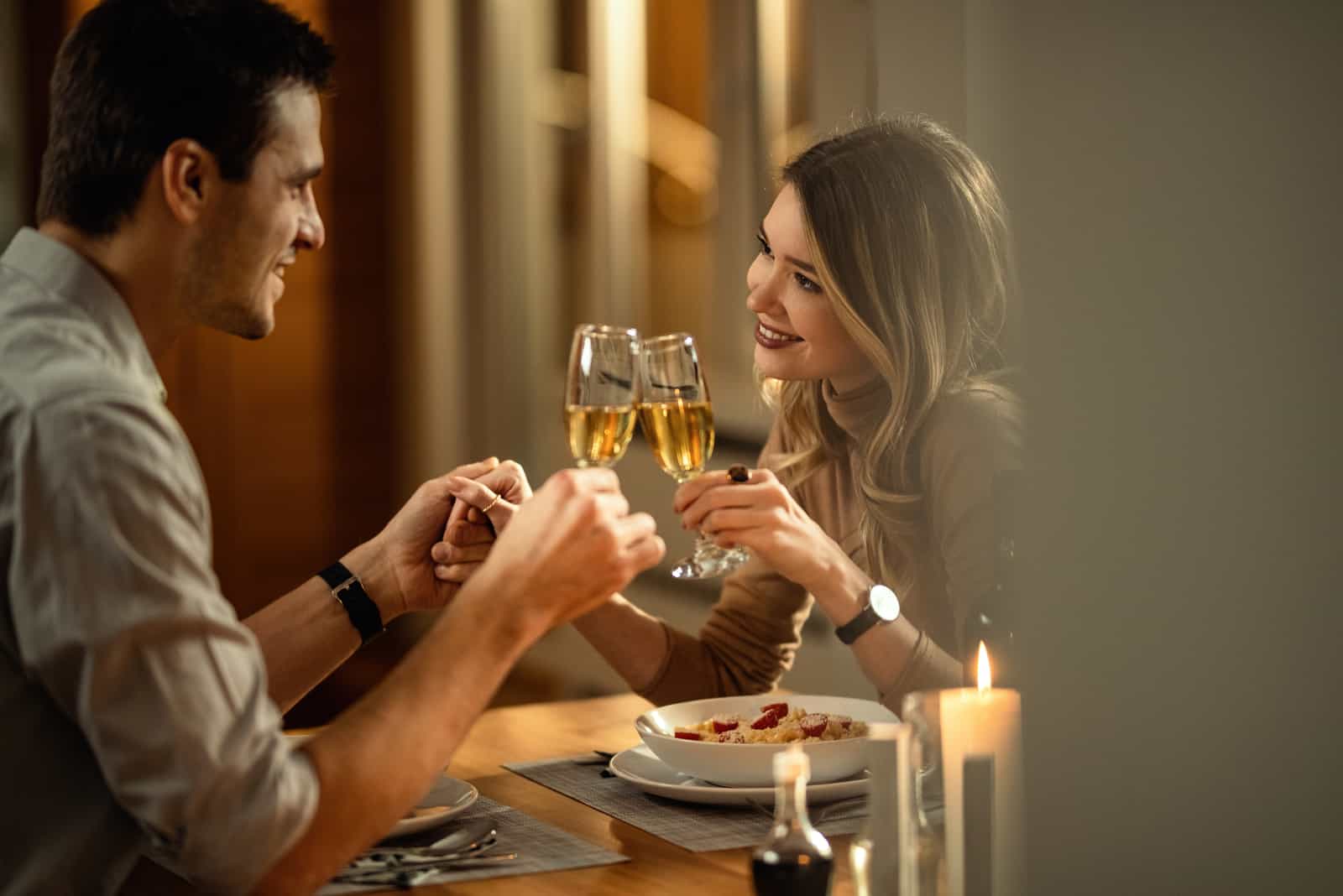 una giovane coppia sorridente che si tiene per mano mentre brinda con lo champagne