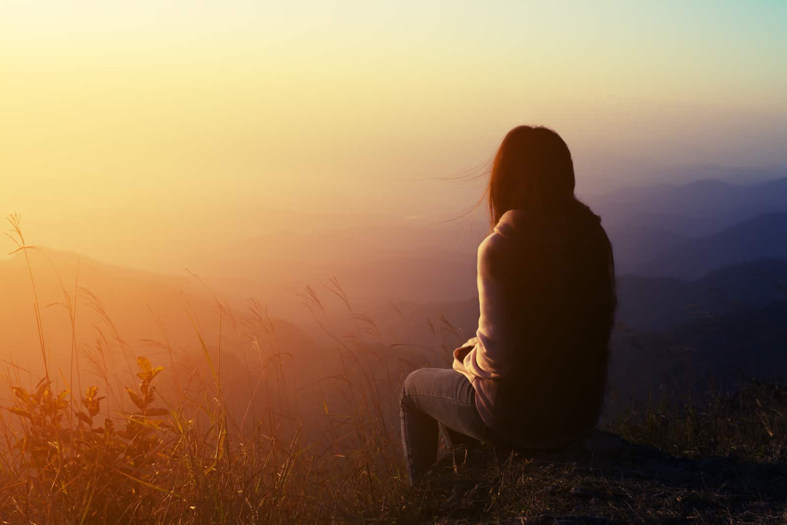 uma mulher imaginária senta-se numa pedra com as costas viradas