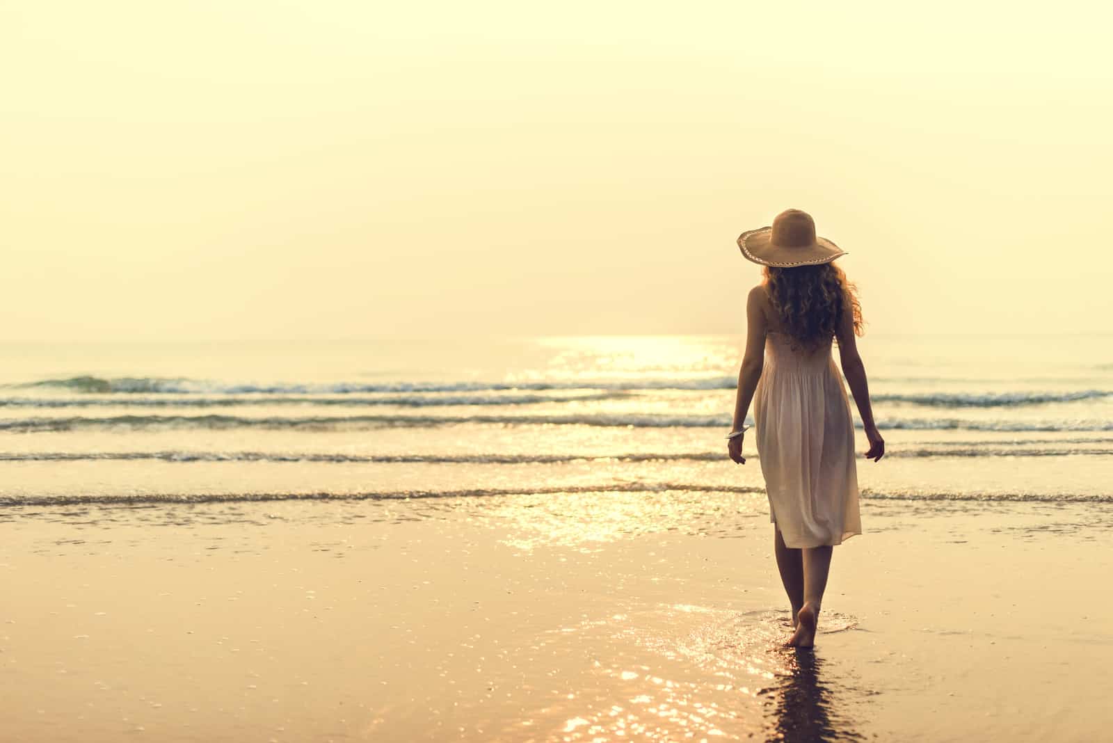 al tramonto una donna scalza in abito bianco cammina sulla spiaggia