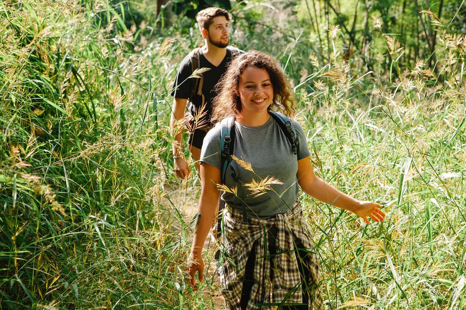 cheerful couple walking between a lush grass while hiking