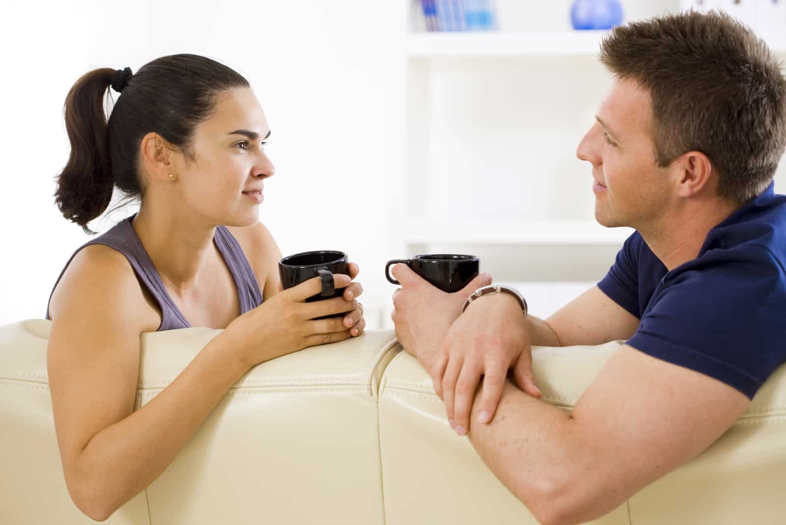 man and woman having coffee while sitting on sofa