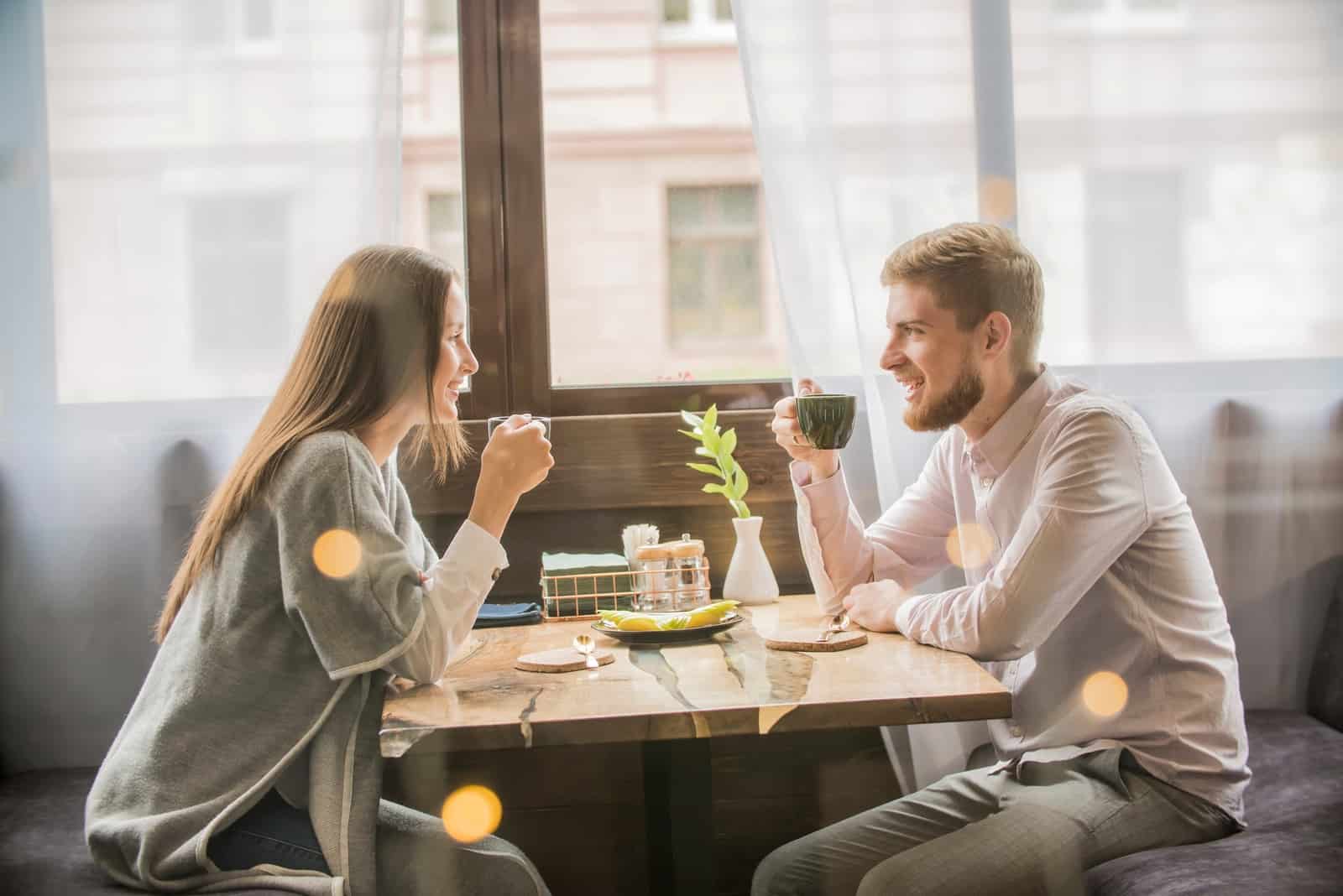 man and woman having coffee while sitting in cafe