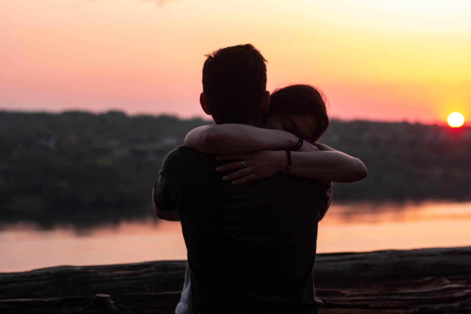 man and woman hugging while standing near water during sunset