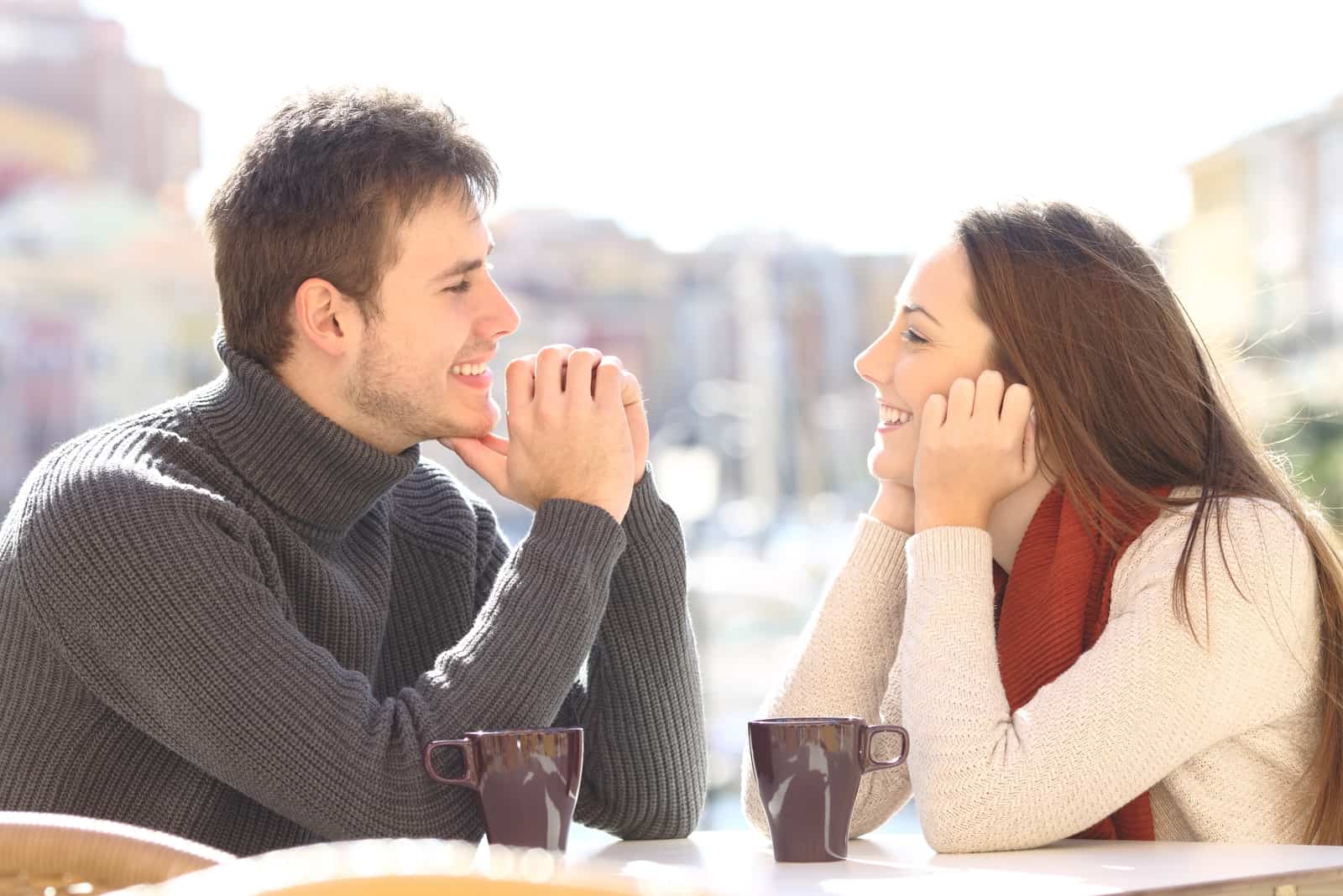 homem e mulher felizes a estabelecerem contacto visual enquanto estão sentados à mesa