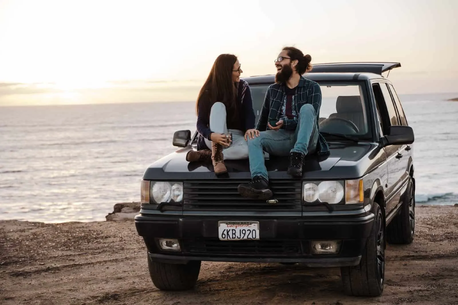 man and woman talking while sitting on car