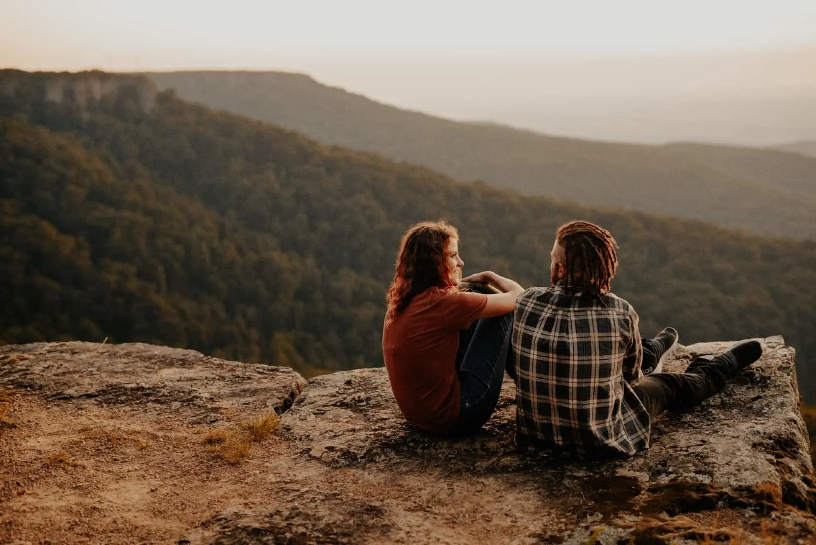 man and woman talking while sitting on rock