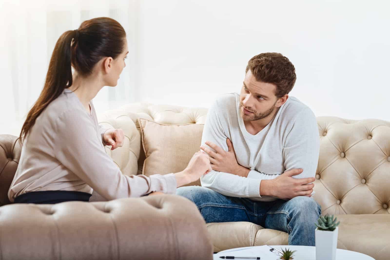 man and woman talking while sitting on sofa