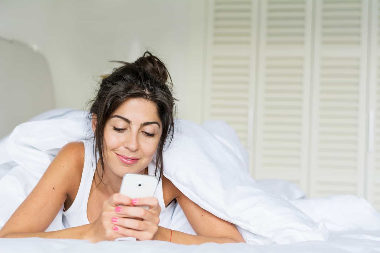 happy brunette in the morning lying in bed and texting