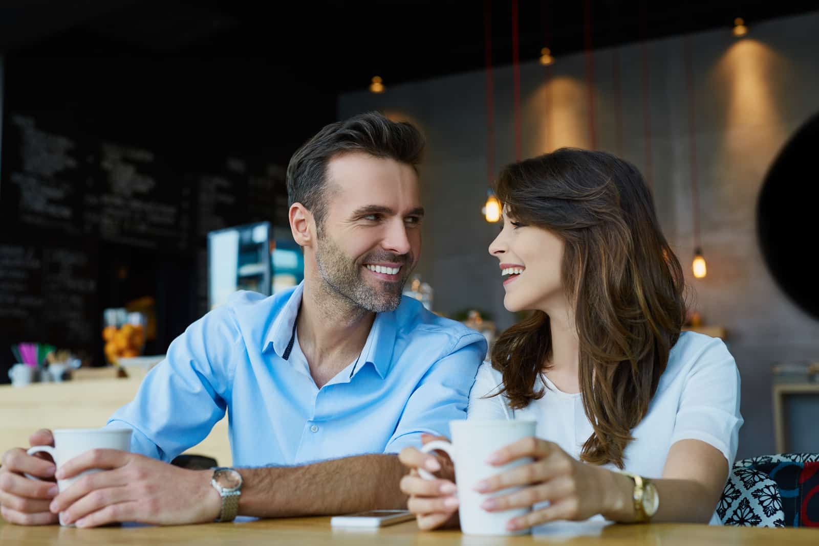 coppia felice seduta in un caffè che ride e si guarda mentre beve il caffè