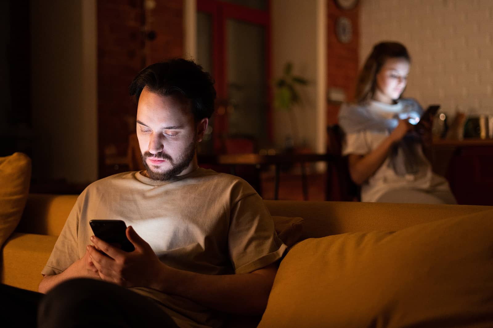 man and a woman using smartphones at home sitting separately places