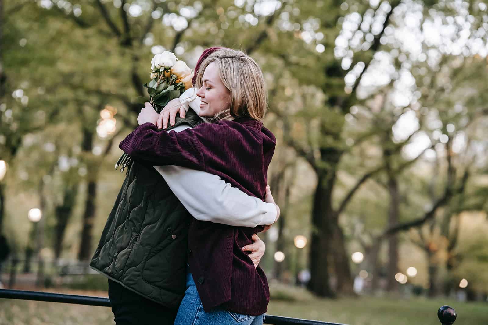 man and woman hugging in the park while woman holding bouquet of white roses