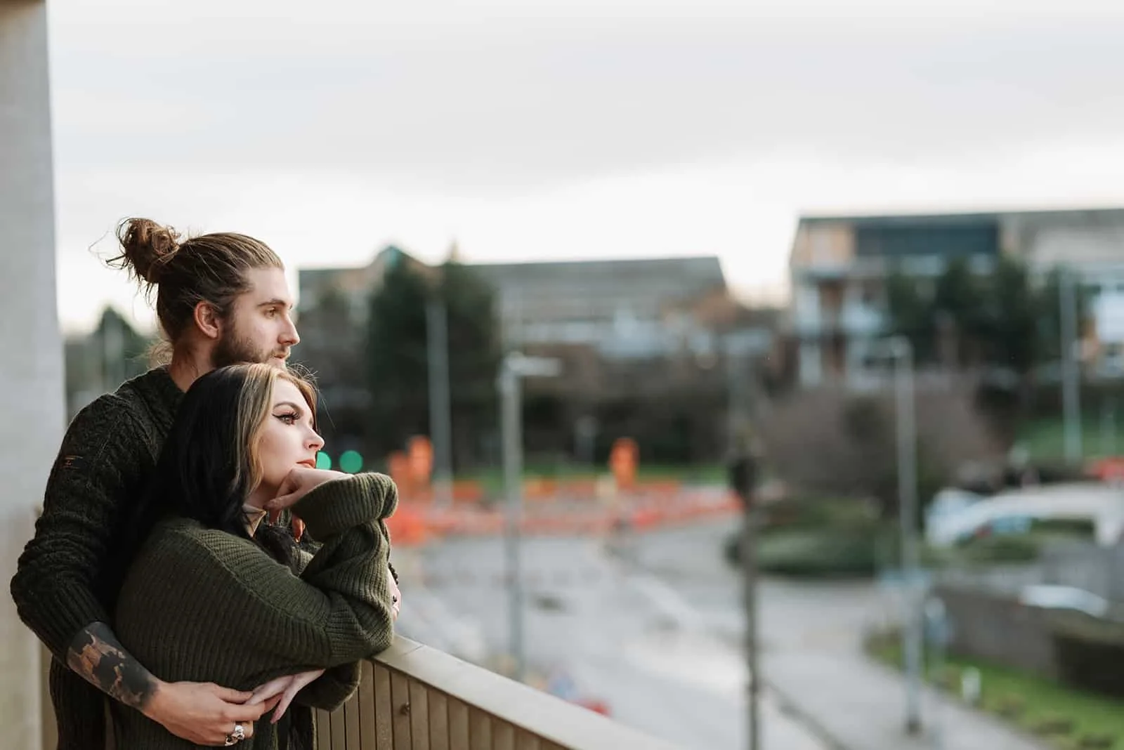 man embracing woman from the back while standing on the terrace and facing the city
