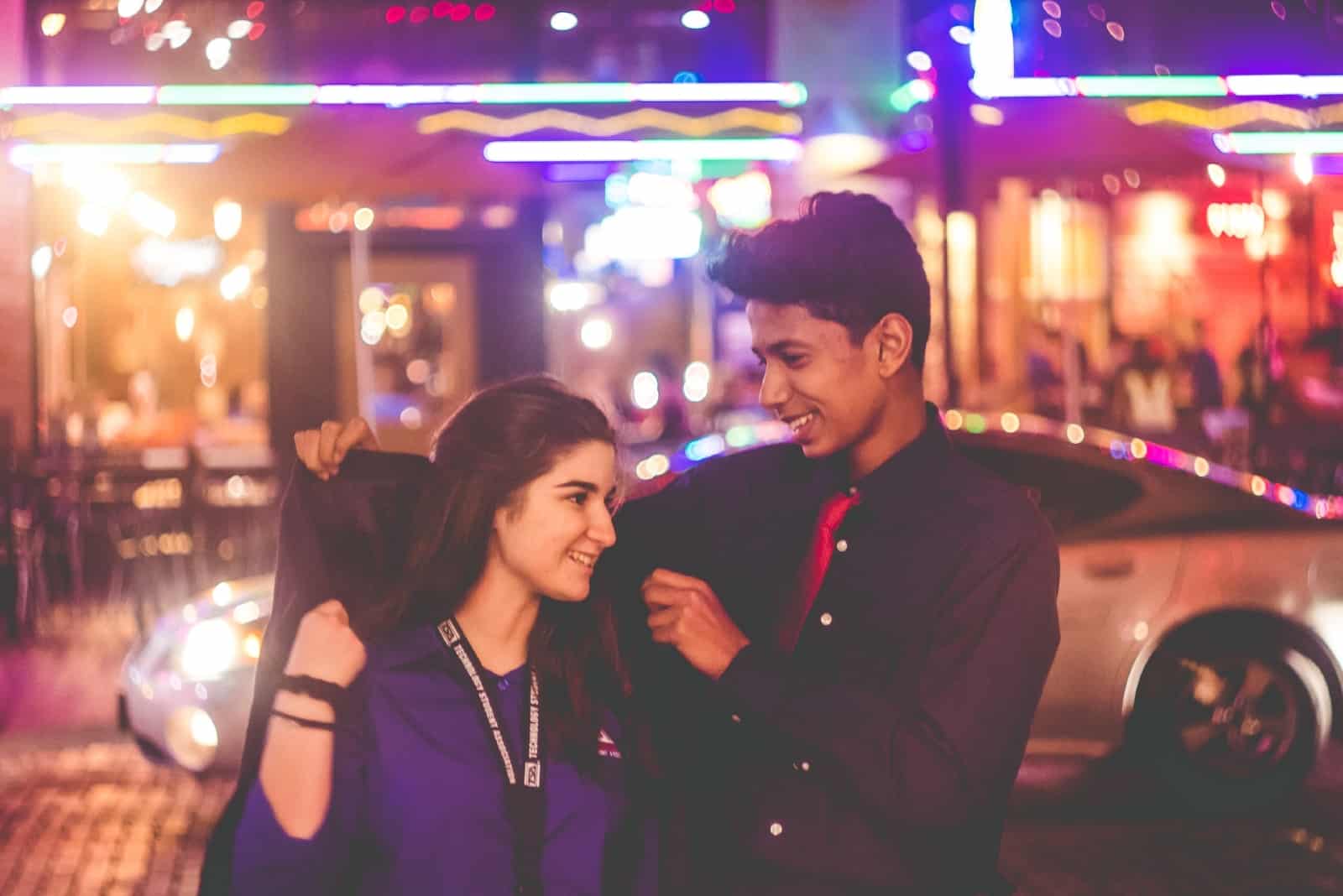 man giving jacket to woman while standing on the street