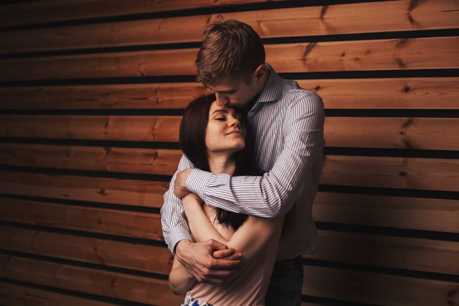 uomo che abbraccia una donna in piedi vicino a una parete di legno
